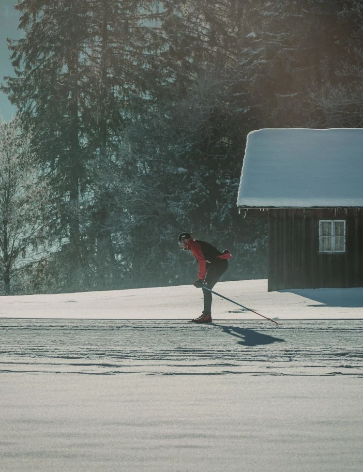 Narciarz biegowy sunący po ośnieżonej łące obok drewnianej chaty, symbolizujący jaworzynka atrakcje zimowe.